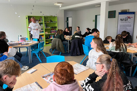 Doreen steht in einem Klassenraum mit einer Gruppe von Schülern und erklärt etwas.