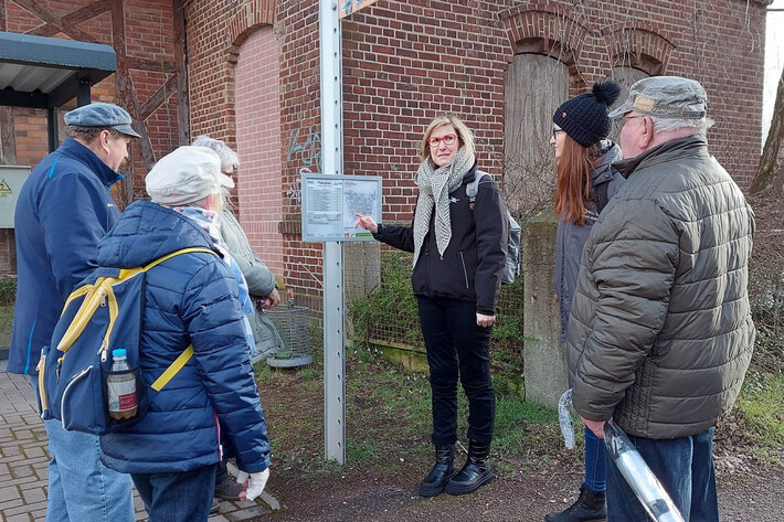 Doreen Havemann steht mit einer Gruppe von erwachenen Menschen an einer Bahnstation und erklärt etwas.