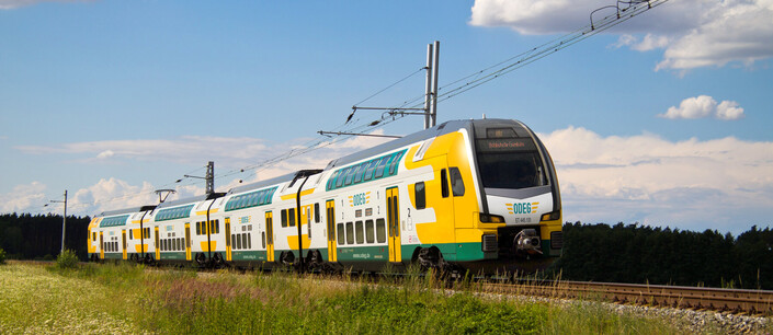Ein grün-gelb-weißer Zug des Typs DESIRO HC in grüner Landschaft
