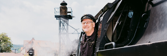 Ein Lokomotivführer schaut aus dem Führerstand einer dampfenden Lok heraus