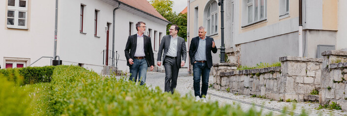 Drei Männer gehen sich unterhaltend an einem Haus vorbei